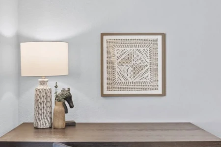 A workspace in the corner of the bedroom includes a desk, a lamp, a picture on the wall, and a cushy gray velvet office chair.