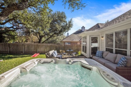 A hot tub offers a serene view of the trees and a charming wooden fence in the backyard.