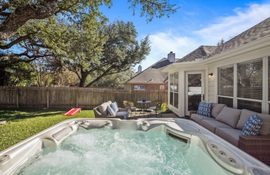 A hot tub offers a serene view of the trees and a charming wooden fence in the backyard.