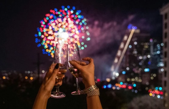 A couple's hand raising a toast with new year's eve fireworks and the city of cedar park at the backdrop