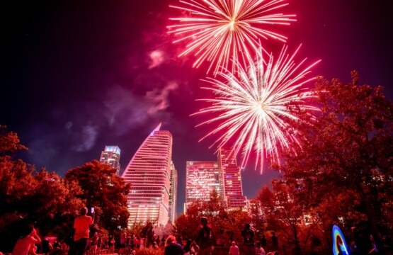 Fireworks display lighting up the night sky during the Cedar Park 4th of July Celebration, with vibrant red and pink bursts over a festive crowd gathered between Cedar Park and Austin, Texas.