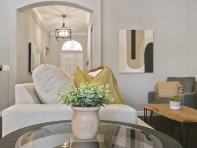 A vase of plants adorns a glass table in the living room, offering a view of the hallway that leads to the front door.