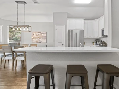 A kitchen countertop with stools, with the dining table and refrigerator in the backdrop.