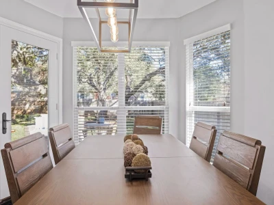 Kitchen table with chairs and a chandelier in front of windows facing the backyard.