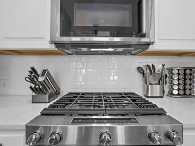 A stylish and aesthetic kitchen with white cabinets, a microwave oven, and a full oven with a gas range.